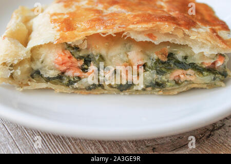 Lo Strudel torta con salmone e spinaci su piastra bianca servita su un tavolo di legno. Vista laterale. Selective soft focus. Foto Stock