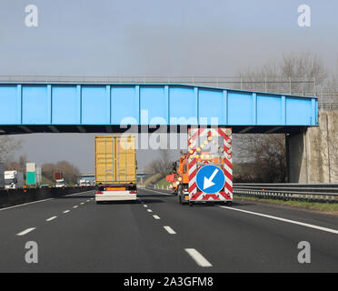 Il sorpasso il carrello in autostrada e il veicolo per indicare lo stato di avanzamento dei lavori con la freccia grande nell'enorme cartello stradale Foto Stock