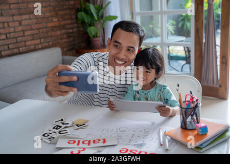 Padre e figlia prendere selfie insieme utilizzando smartphone durante lo studio Foto Stock