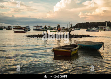 Vista orizzontale di tre pescatori (Tres isole Pescadores) scultura e imbarcazioni a Buzios, Brasile durante il tramonto su un nuvoloso giorno di estate Foto Stock