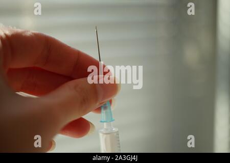Mano femmina trattiene una siringa con un ago foto sfocata. Foto Stock