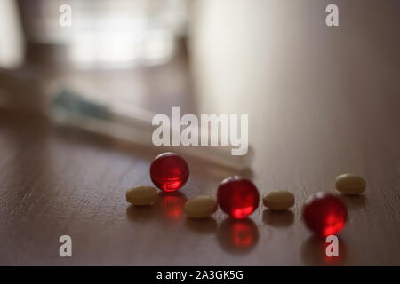 Pillole e vitamine rosso. Siringa e acqua in vetro sfondo sfocato. Il trattamento e il recupero, la dieta o la tossicodipendenza. Foto Stock