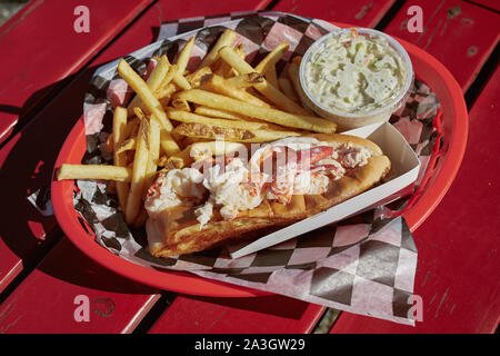 Mangiare tradizionale Maine lobster roll con coleslaw e patatine fritte su un lungomare porto nel Maine. Foto Stock