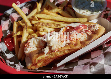 Mangiare tradizionale Maine lobster roll con coleslaw e patatine fritte su un lungomare porto nel Maine. Foto Stock