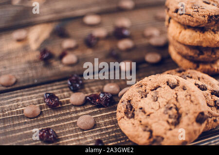 Una pila di fiocchi d'avena i biscotti con pezzetti di cioccolato e frutta candita giace su di un tavolo di legno. Tavolo rustico. Tonificazione vintage. Integratore utile i cookie Foto Stock