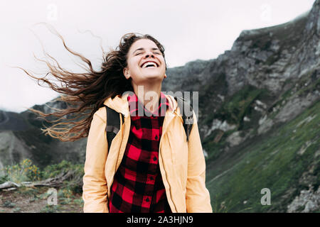 Bella tanga caucasica ragazza con lunghi capelli ricci gode del battente sulla cima di una montagna. Foto Stock