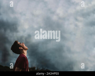 Teen boy guardando il cielo nuvoloso scuro con la sua bocca spalancata. Foto Stock