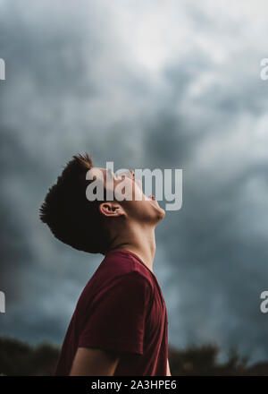 Teen boy guardando il cielo nuvoloso scuro con la sua bocca spalancata. Foto Stock