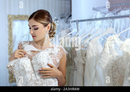 Bella giovane donna misure abiti da sposa in un salone. Foto Stock