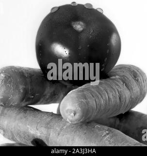 Un pomodoro su alcune carote. Foto in bianco e nero. Foto Stock