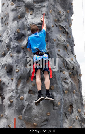 Ragazzo adolescente scalare la parete di arrampicata che indossa il cablaggio e le cinghie di sicurezza presso il St Thomas University speciale evento olimpico. St Paul Minnesota MN USA Foto Stock