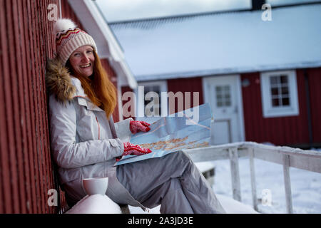 Felice ragazza turistica si siede vicino rorbu con una mappa a isole Lofoten. Norvegia Foto Stock