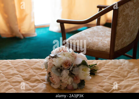 Un bellissimo mazzo di nozze di peonie e rose giacente sul letto in appartamento per preparare la sposa per la celebrazione delle nozze e expecta Foto Stock