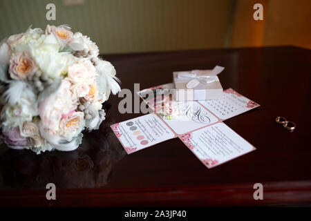 Wedding bouquet di peonie e rose giacente su un vintage in legno tavolo vicino gli anelli di nozze sullo sfondo del bando negli appartamenti di prepa Foto Stock