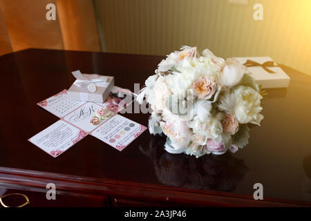 Wedding bouquet di peonie e rose giacente su un vintage in legno tavolo vicino gli anelli di nozze sullo sfondo del bando negli appartamenti di prepa Foto Stock