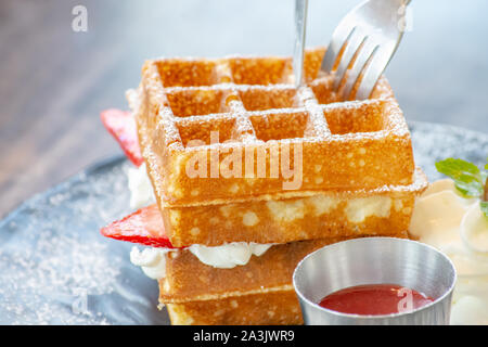 Waffle Strawerry panna fresca nella piastra nera su un tavolo di legno. Foto Stock