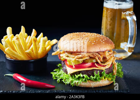 Close-up di Cheeseburger con polpetta di carne, formaggio cheddar, croccante di cipolle fritte, lattuga, pomodori a fette, sottaceti sul bordo di pietra con patatine fritte e Foto Stock