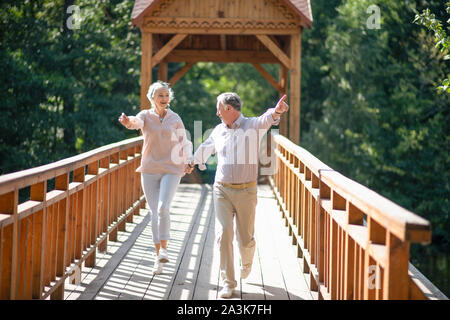 Adulti maturi in esecuzione mentre si attraversa il ponte e la sensazione di essere eccitato Foto Stock