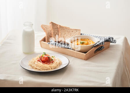 In casa spaghetti con sugo di pomodoro collocato in un piatto bianco sul tavolo con purea di zucca, latte e pane tostato. Foto Stock