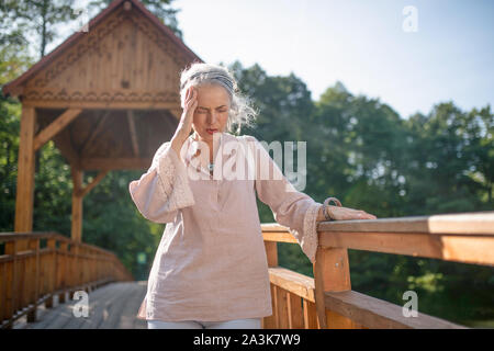 La donna che soffre di mal di testa mentre passeggiate nel parco Foto Stock