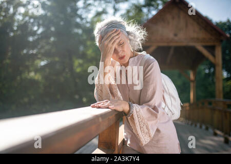 Grigio-dai capelli donna con mal di testa mentre si cammina Foto Stock