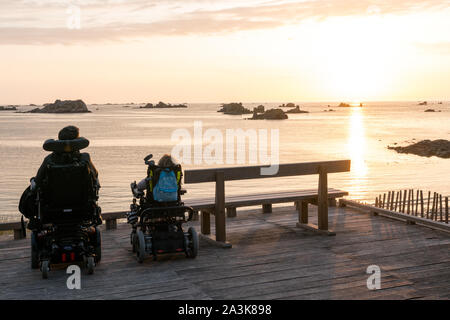 Roscoff, Finisterre / Francia - 21 agosto 2019: due persone in carrozzina godere la possibilità di guardare il tramonto sulla spiaggia e l'oceano Foto Stock