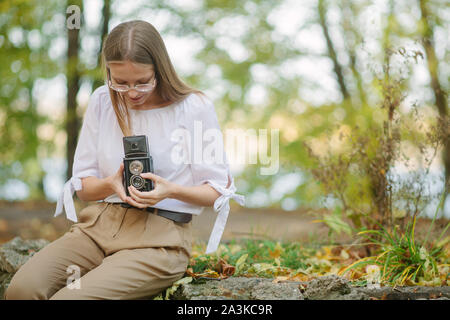 Attraente bella ragazza giovane azienda retro vintage doppia lente della fotocamera di riflessione nell'autunno del parco. Foglie di giallo sul pavimento e lo sfondo Foto Stock