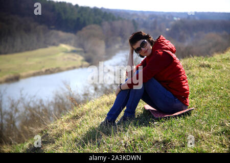 Una ragazza raccoglie snowdrops nella foresta. Bella giovane donna bagna i raggi del sole di primavera in una radura della foresta. Foto Stock