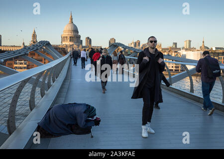 Pedoni camminare davanti a un mendicante sul Millennium Bridge con la Cattedrale di St Paul e oltre, London, England, Regno Unito Foto Stock