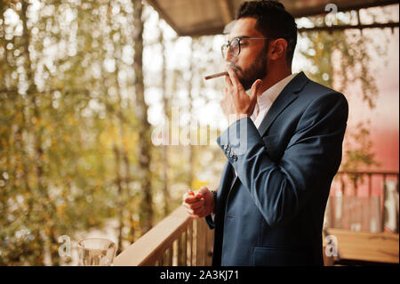 Bello e ben vestito uomo arabo di fumo di sigaro balcone di pub. Foto Stock