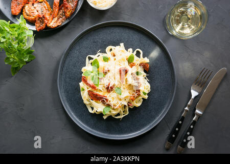 Tagliatelle di pasta con pomodori secchi e origano su sfondo nero. Delizioso pranzo mediterraneo. Vista dall'alto. Foto Stock