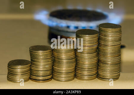 Aumento del prezzo del gas concetto. Blu fiamma a gas e aumentando la pila di monete. Simbolo di aumento dei costi del gas. Foto Stock