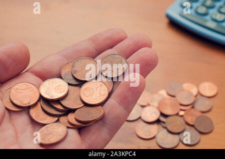 Man tenere una buch di due euro cent nel palmo della sua mano su una tabella con altre monete e di una calcolatrice Foto Stock