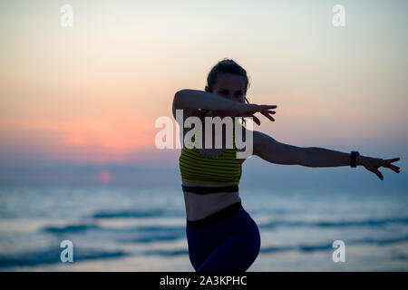 Silhouette di sport fitness donna in abiti sportivi sulla costa dell'oceano in serata facendo arti marziali formazione. Foto Stock