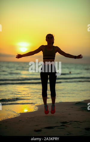 Silhouette di active sport donna in abiti sportivi sulla spiaggia al tramonto facendo HIIT allenamento. Foto Stock