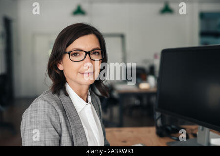 Imprenditrice sorridente seduto alla sua scrivania in un ufficio Foto Stock