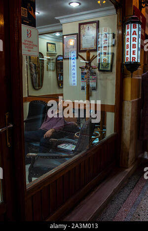 Istanbul: uomo di dormire su una sedia in un Barber shop all'interno del Cicek Pasaji, il passaggio di fiori, la storica galleria su Istiklal Caddesi, una famosa avenue Foto Stock