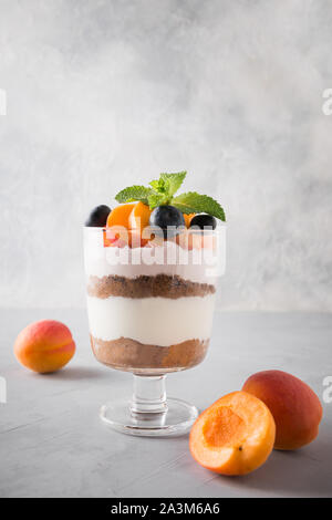 Albicocca inezia, biscotti al cioccolato, dessert a strati con bacche fresche e dolci crema di formaggio su sfondo grigio. Messa a fuoco selettiva. Colpo verticale. Foto Stock