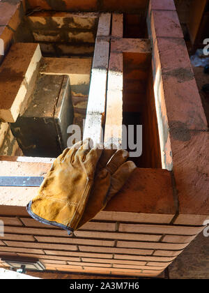 La stufa funzionante gauntlets giacciono sul bordo del rosso mattone di argilla stufa. Guanti da lavoro. Foto Stock