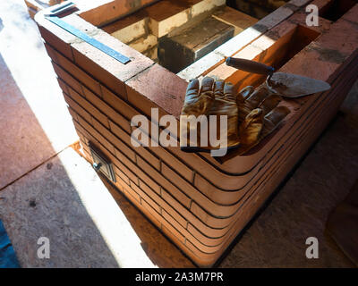 La stufa funzionante gauntlets giacciono sul bordo del rosso mattone di argilla stufa. Guanti da lavoro. Foto Stock