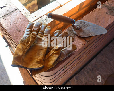 La stufa funzionante gauntlets giacciono sul bordo del rosso mattone di argilla stufa. Guanti da lavoro. Foto Stock