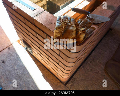 La stufa funzionante gauntlets giacciono sul bordo del rosso mattone di argilla stufa. Guanti da lavoro. Foto Stock