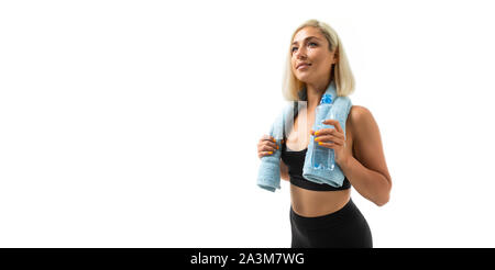 Un sport giovane ragazza con i capelli biondi in uno sport di ax e gambali nero detiene un asciugamano blu e una bottiglia di acqua. Foto Stock