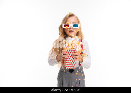 Una bambina con lunghi capelli biondi gli occhiali 3-D mangiare popcorn. Foto Stock