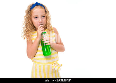 Una bambina con il rosso dei capelli di heap in un bianco e giallo listati estate suit, con un bendaggio blu sul suo capo le bevande di succo d'arancia in una bottiglia di vetro di Foto Stock