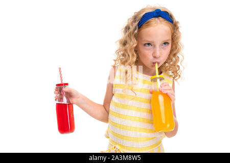 Una bambina con il rosso dei capelli di heap in un bianco e giallo listati estate suit, con un bendaggio blu sul suo capo le bevande di succo d'arancia in una bottiglia di vetro di Foto Stock
