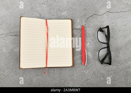 Notebook nero e rosso penna. Blank notebook e penna rossa. Blank notebook e penna rossa sul cemento grigio Sfondo. vista dall'alto. Foto Stock