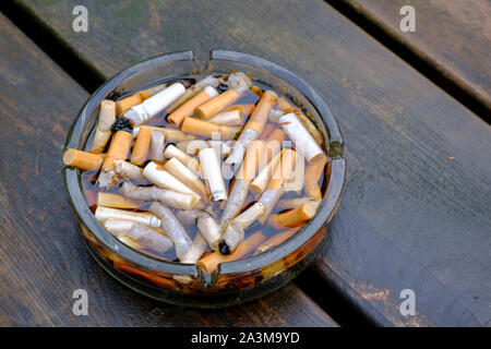 Posacenere pieno di mozziconi di sigarette su una tabella dopo la pioggia Foto Stock