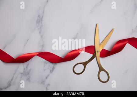 Inaugurazione dello sfondo. Forbici di oro con nastro rosso su sfondo marmo Foto Stock