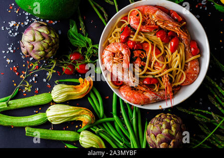 Deliziosi piatti di pasta italiana con gamberoni o gamberetti e verdure fresche su sfondo nero. Una sana dieta mediterranea concetto. Foto Stock